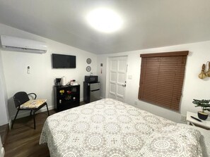 Une chambre à coucher comprenant un lit, un bureau, une chaise, un téléviseur et une fenêtre avec des stores.