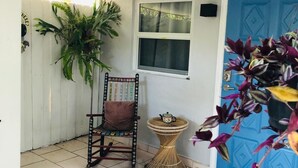A room with a white tiled floor, a blue door, a window, a chair, a small table, and a potted plant.