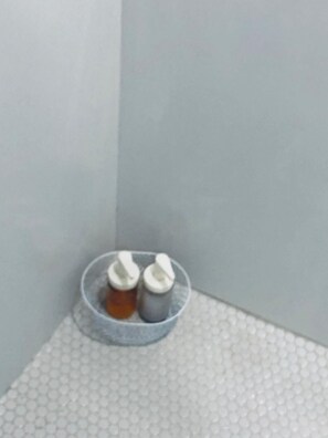 Un coin de pièce avec un sol blanc à texture et un autre coin où se trouve une petite table ronde sur laquelle reposent deux bouteilles.