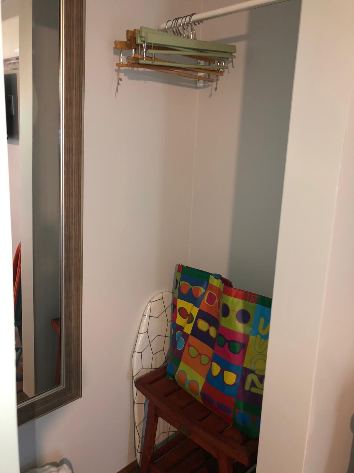A bathroom with a wooden bench, a colorful shower curtain, and a mirror.