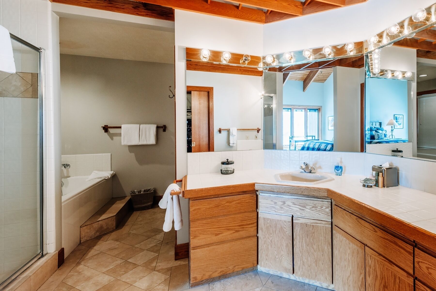 Un baño con bañera, lavabo, espejo con luces, armarios de madera y un perchero para toallas.