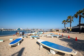 Una spiaggia con diversi surf oramai disposti sulla sabbia, alcune palme e un cielo azzurro terso.