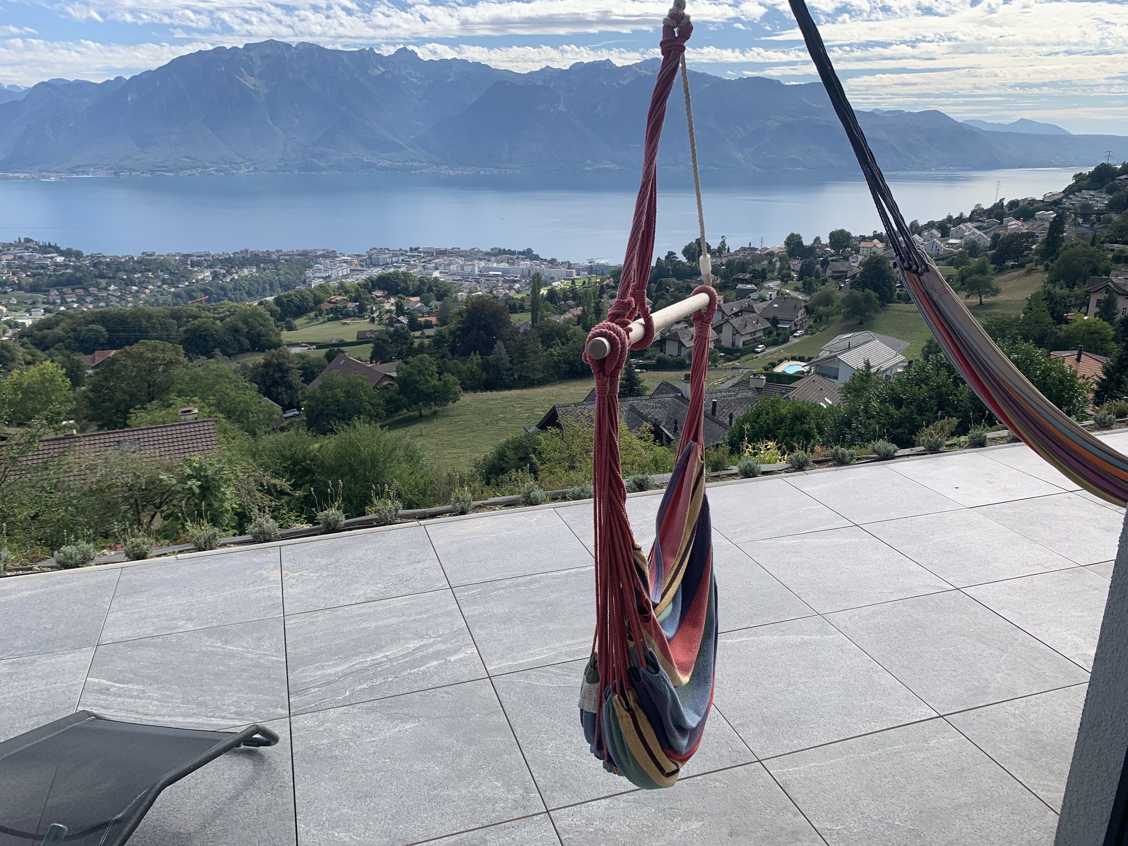 Una hamaca en un patio con baldosas con vistas a un lago y montañas.