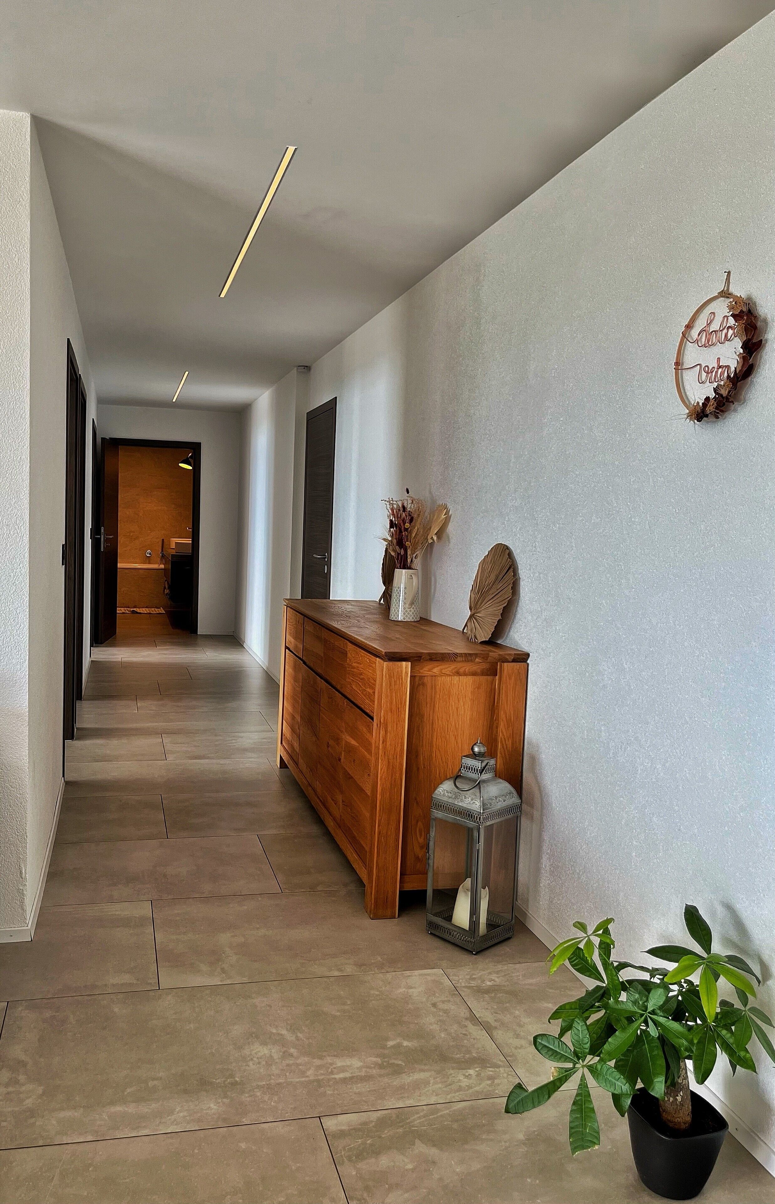 A hallway with a wooden bench, a potted plant, and a decorative wall hanging.