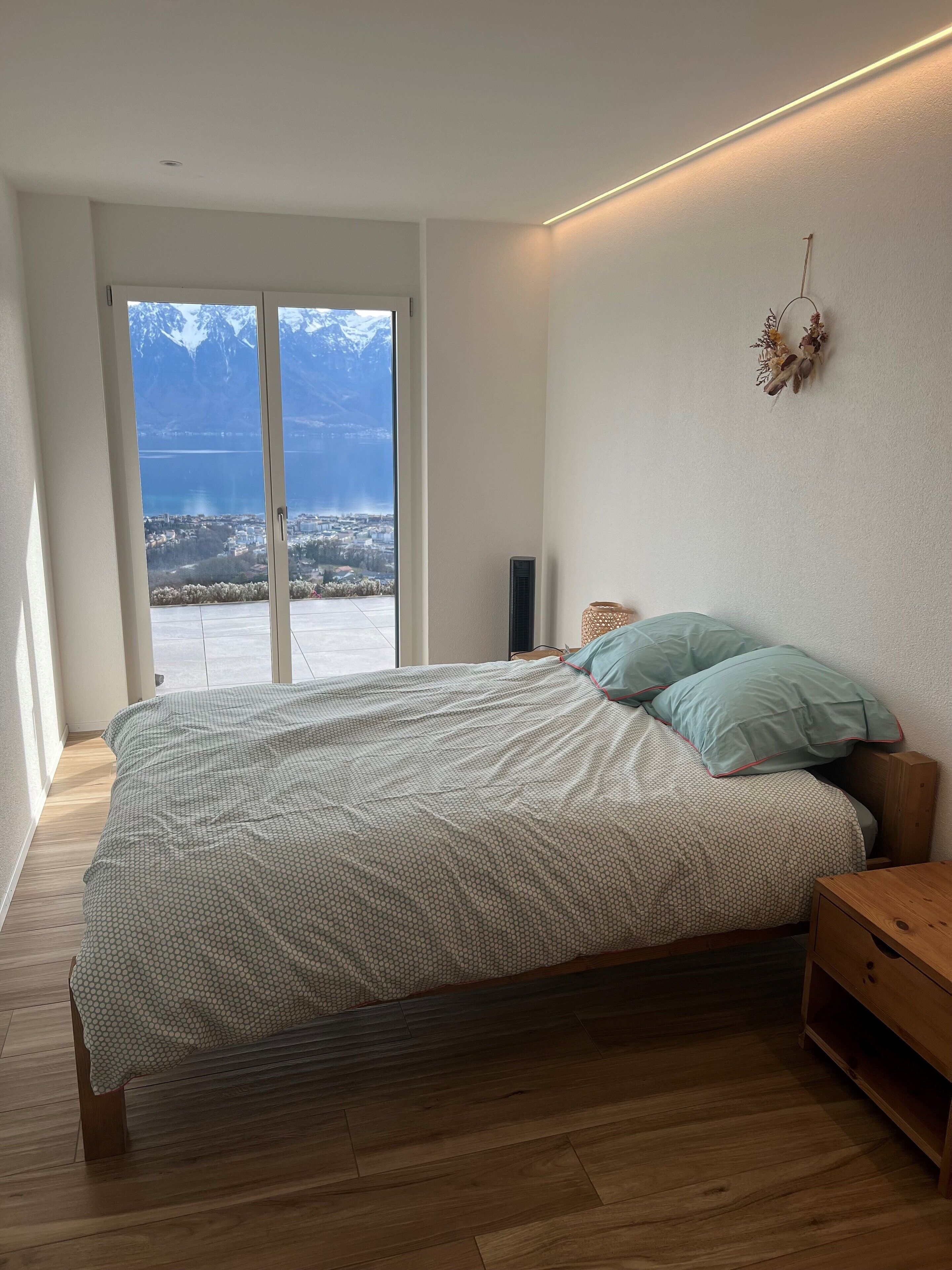 Ein Schlafzimmer mit Bett, Holzboden, Blick auf Berge und See sowie einem Wandheizkörper.
