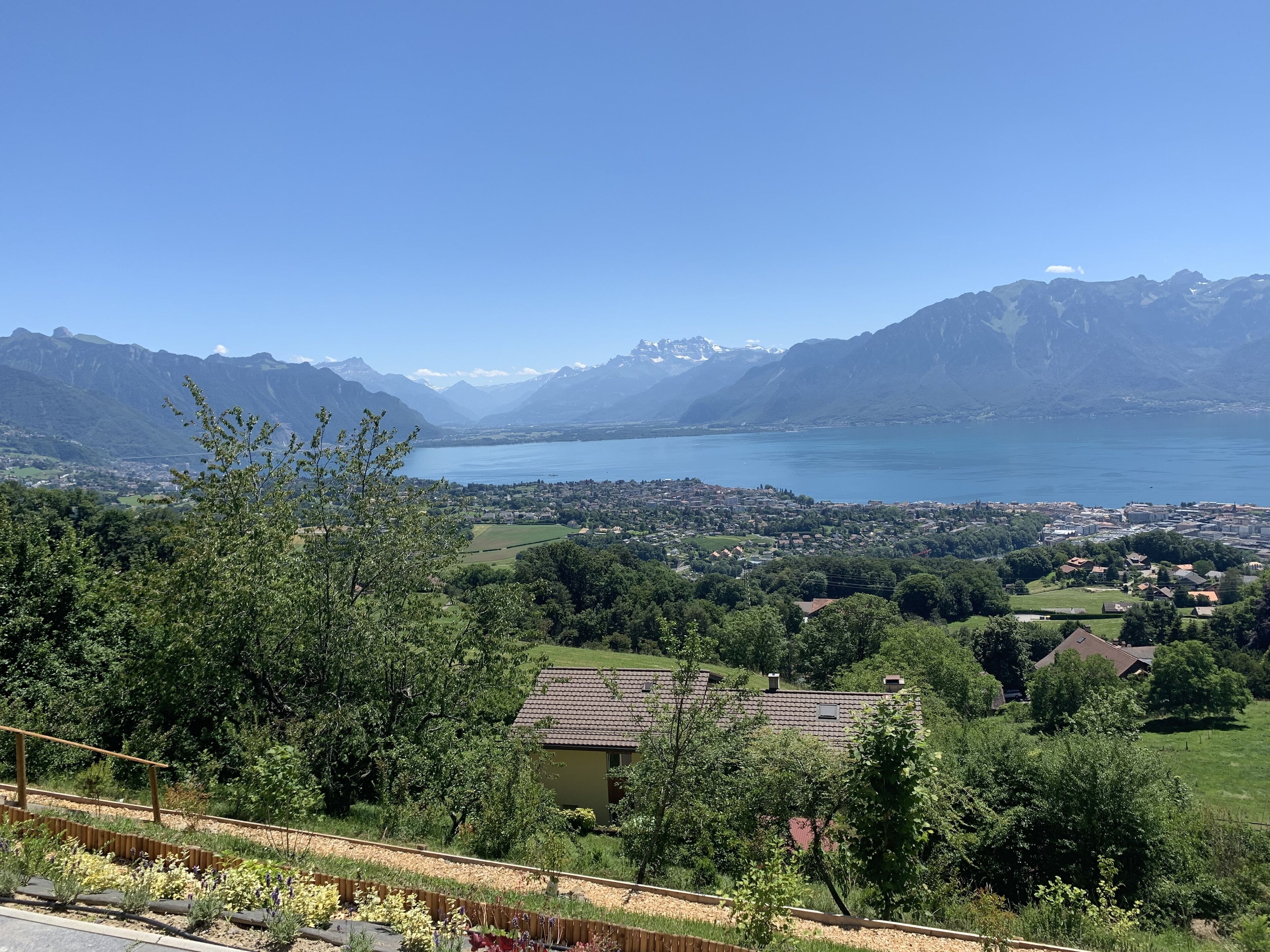 A scenic view of a lake surrounded by mountains, with a town in the foreground and a clear sky.