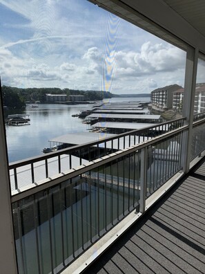 A view from a balcony overlooking a marina with boats docked, a river, and buildings in the background.