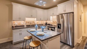 A modern kitchen with white cabinets, a stainless steel refrigerator, and a central island with stools. - Luxury Living in Downtown Provo Unit 2 (Provo)
