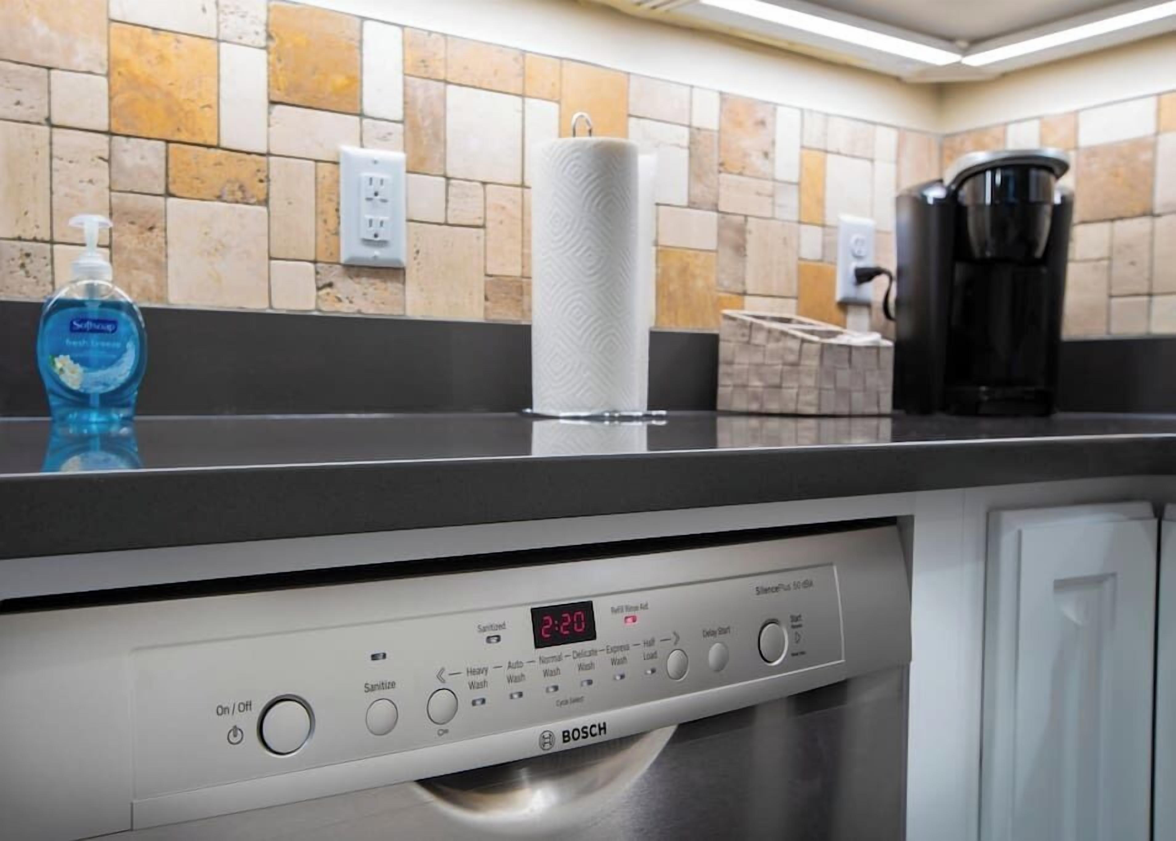 Un lavavajillas Bosch con pantalla digital, un dispensador de detergente y un porta paños de cocina sobre una encimera.
