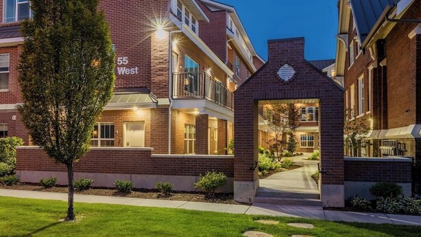 A multi-story brick building with a well-lit entrance, a small tree in the foreground, and a clear pathway leading to the entrance. - Luxury Living in Downtown Provo Unit 2 (Provo)