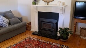 A living room with a fireplace, a grey sofa, a red patterned rug, and a television on a wooden stand.