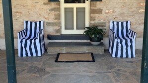 A stone building with a white door, two striped chairs, and a potted plant on the steps.