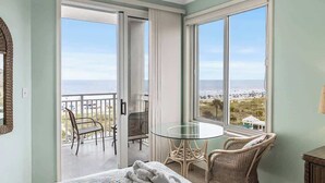Una habitació amb un llit, una taula de vidre, cadires de vimetes i un balcó amb vista a la platja.