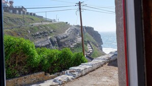 Vista costera a través de una ventana, con un camino de piedra que lleva al borde de un acantilado.