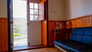Una habitación con piso de madera, un sofá azul, una puerta de madera y vistas a zonas verdes al exterior.