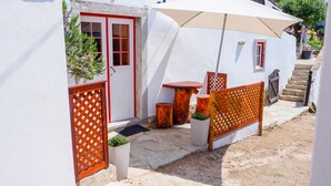 Un edificio blanco con una puerta roja, una valla de madera y una mesa con un banco.