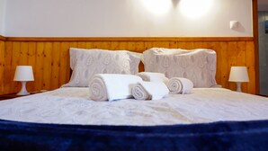 Una cama bien hecha con toallas enrolladas, un cabecero de madera y dos lámparas de noche.