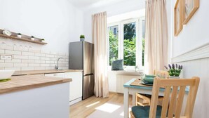 A modern kitchen with white cabinetry, a stainless steel refrigerator, and a window with curtains. - Stylish Studio in Mokotow | Close to Metro and Parks (Warszawa)