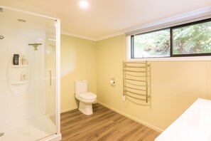Une salle de bain avec une douche à parois de verre, des toilettes, un porte-serviettes et une fenêtre donnant sur un espace verdoyant.