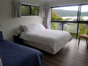 Une chambre à coucher avec un lit, une table de chevet, une lampe et une chaise. Il y a une fenêtre qui donne sur un lac et des collines.
