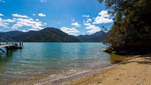 A lake with a dock and a sandy beach. - 🌿 Birdsong Hideaway 🌿 (Moetapu Bay)