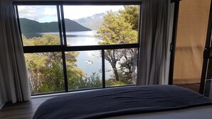 A bedroom with a large window overlooking a lake and mountains. - 🌿 Birdsong Hideaway 🌿 (Moetapu Bay)