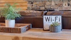 En inredning med trädetaljer och en öppen spis i sten, en brun lädersoffa, ett träbord och en krukväxt, samt en skylt med texten ”Wi-Fi”.