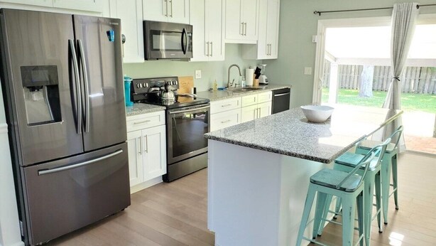 A modern kitchen with white cabinets, stainless steel appliances, and a central island with bar stools. - Pet-Friendly 3BR Private Home with Pool Near Beach (St. Augustine)