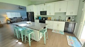 A modern kitchen with white cabinets, a granite countertop, and a central island with bar stools. - Pet-Friendly 3BR Private Home with Pool Near Beach (St. Augustine)