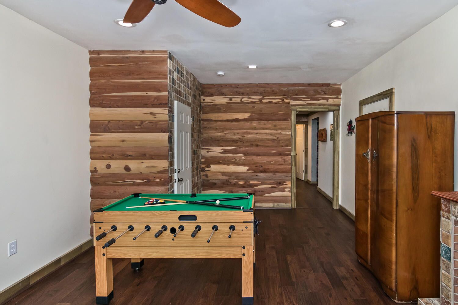 A hallway with a pool table, wooden walls, and a wooden wardrobe.