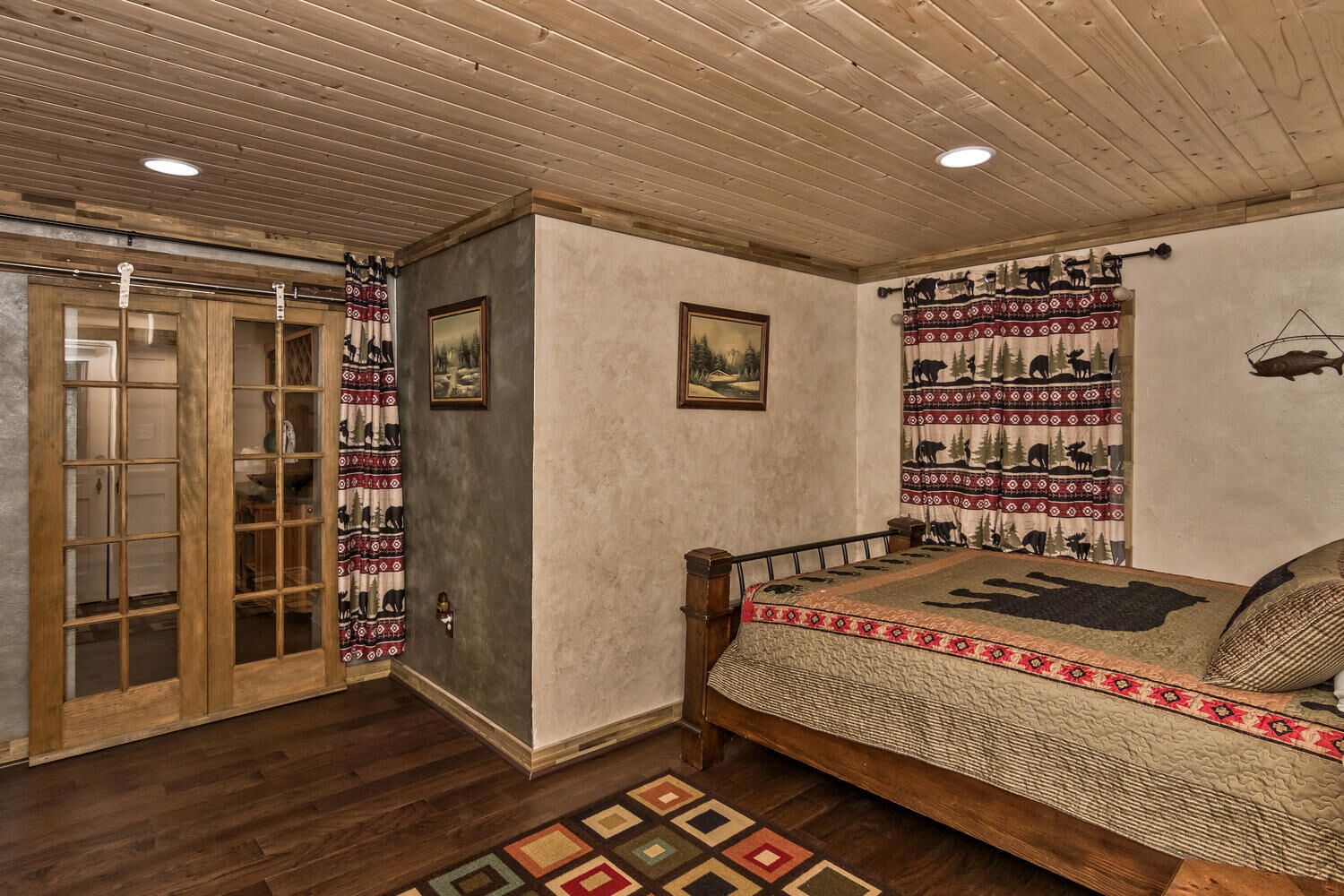 Un dormitorio con techo de madera, una cama con cubrecama estampado, una puerta con paneles de vidrio y una pared con un tapiz que representa animales.