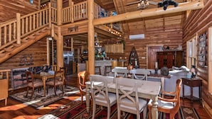 Interior espacioso de una cabaña de madera con comedor, cocina y una escalera que sube a un nivel superior.