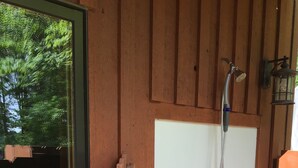Una cabaña de madera con una puerta blanca, ducha y ventana.