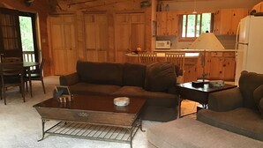 Interior acogedor de una cabaña con una mesa de comedor de madera, un sofá y una zona de cocina con microondas y refrigerador.