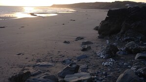 Een strand met grote rotsen op de voorgrond en een ondergaande zon op de achtergrond.