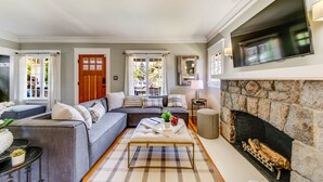A living room with a sofa, a coffee table, a fireplace, and a television mounted on the wall. - The Proctor House: North End, Old Town, Ruston (Tacoma)