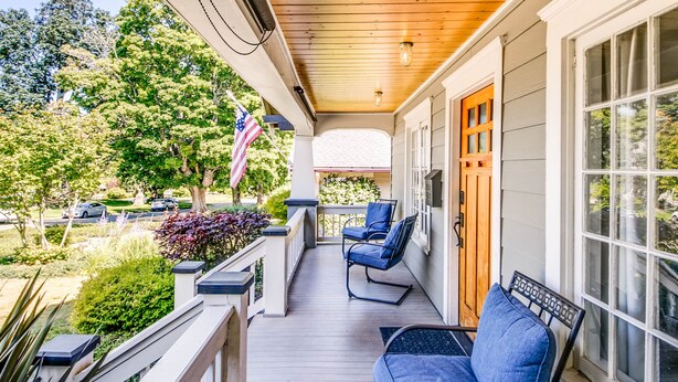 A covered porch with wooden flooring, a railing, and two blue chairs. - The Proctor House: North End, Old Town, Ruston (Tacoma)