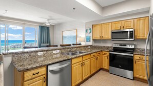 A kitchen with granite countertops, wooden cabinets, stainless steel appliances, a dishwasher, and a view of the ocean. - Ariel Dunes II 1206 - Gulf Views, Heated Community Pool, Steps to the Beach! (Miramar Beach)