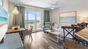 A hotel room with a balcony, a dining area, a sofa, and a painting of the ocean. - Ariel Dunes II 1206 - Gulf Views, Heated Community Pool, Steps to the Beach! (Miramar Beach)