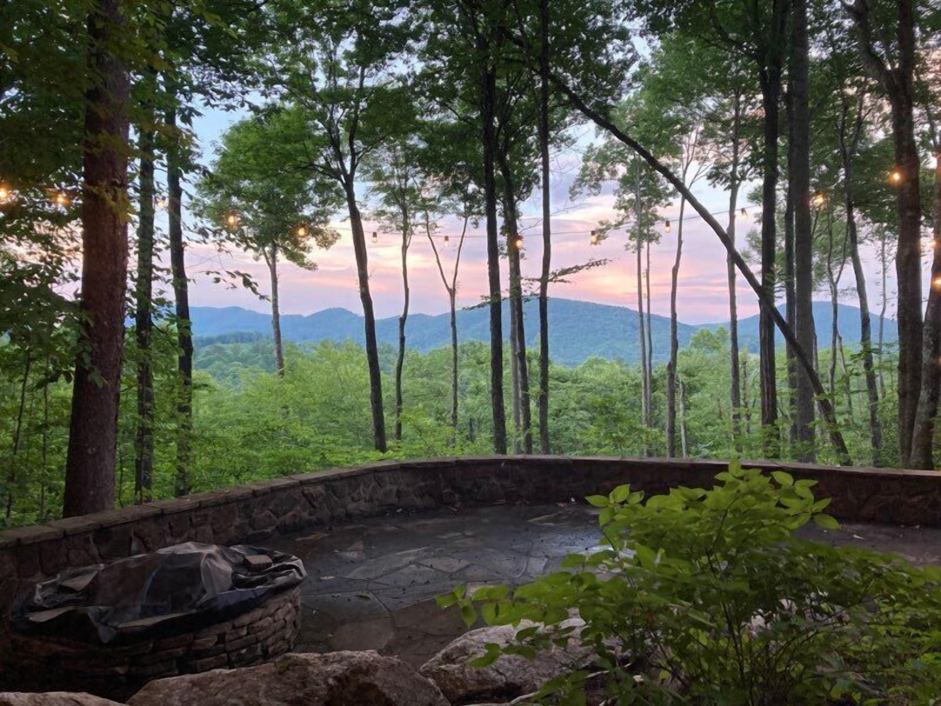 Une terrasse en pierre avec un barbecue, entourée d’arbres et offrant une vue sur les montagnes lointaines.