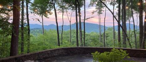 Une terrasse en pierre avec un barbecue, entourée d’arbres et offrant une vue sur les montagnes lointaines.