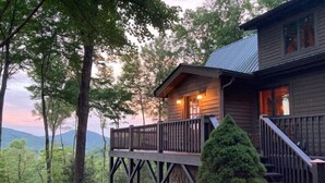 Une cabane en bois dotée d’un balcon, entourée d’arbres et avec une chaîne de montagnes en arrière-plan.