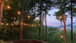 Un bain à remous revêtu de pierres, entouré d’arbres, avec des guirlandes lumineuses suspendues au-dessus.