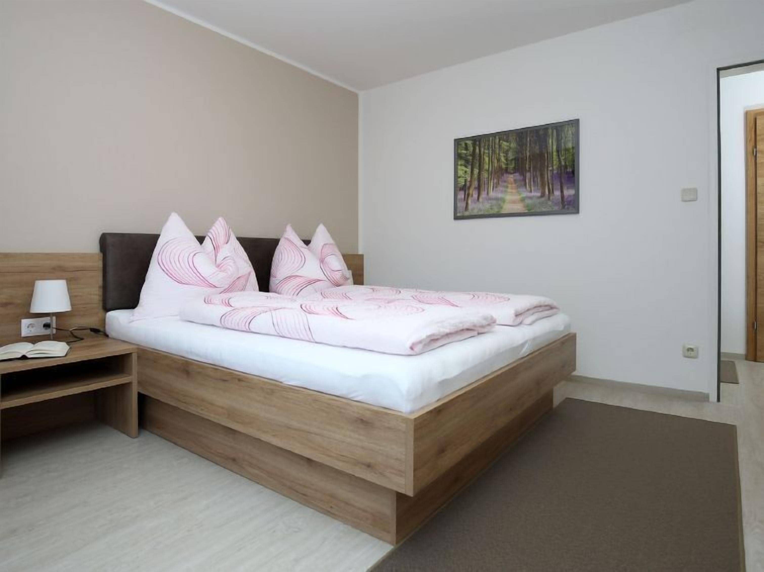 Ein Schlafzimmer mit einem hölzernen Bett, weißer Bettwäsche, einem Nachttisch mit Lampe und einem Gemälde an der Wand.