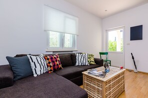 A modern living room with a sectional sofa, a wooden coffee table, and a window with blinds.