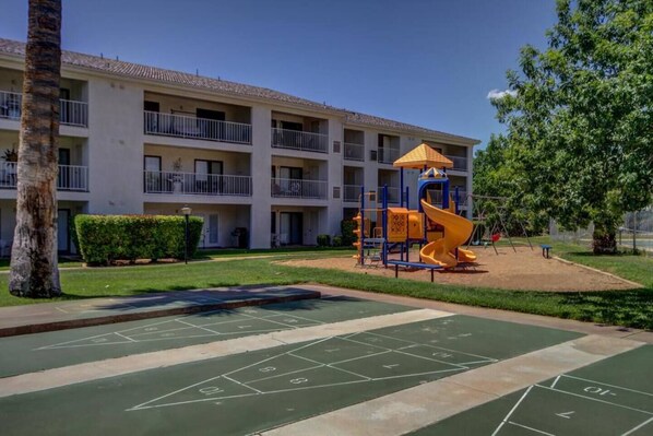A courtyard with a playground, a shuffleboard court, and a multi-story building with balconies. - Newly Renovated St. George Getaway!! (St. George)