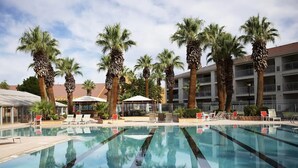 A swimming pool with lounge chairs and palm trees, surrounded by a building with balconies. - Newly Renovated St. George Getaway!! (St. George)