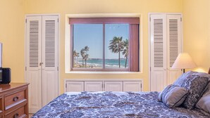Ein Schlafzimmer mit einem großen Fenster und Blick auf den Strand und Palmen.