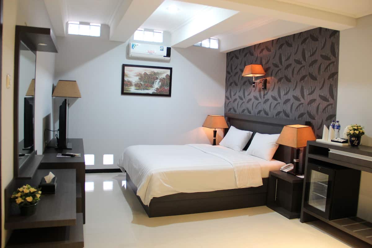 A modern hotel room with a large bed, two bedside lamps, a small table with a lamp, a mirror, and a wall-mounted air conditioner.