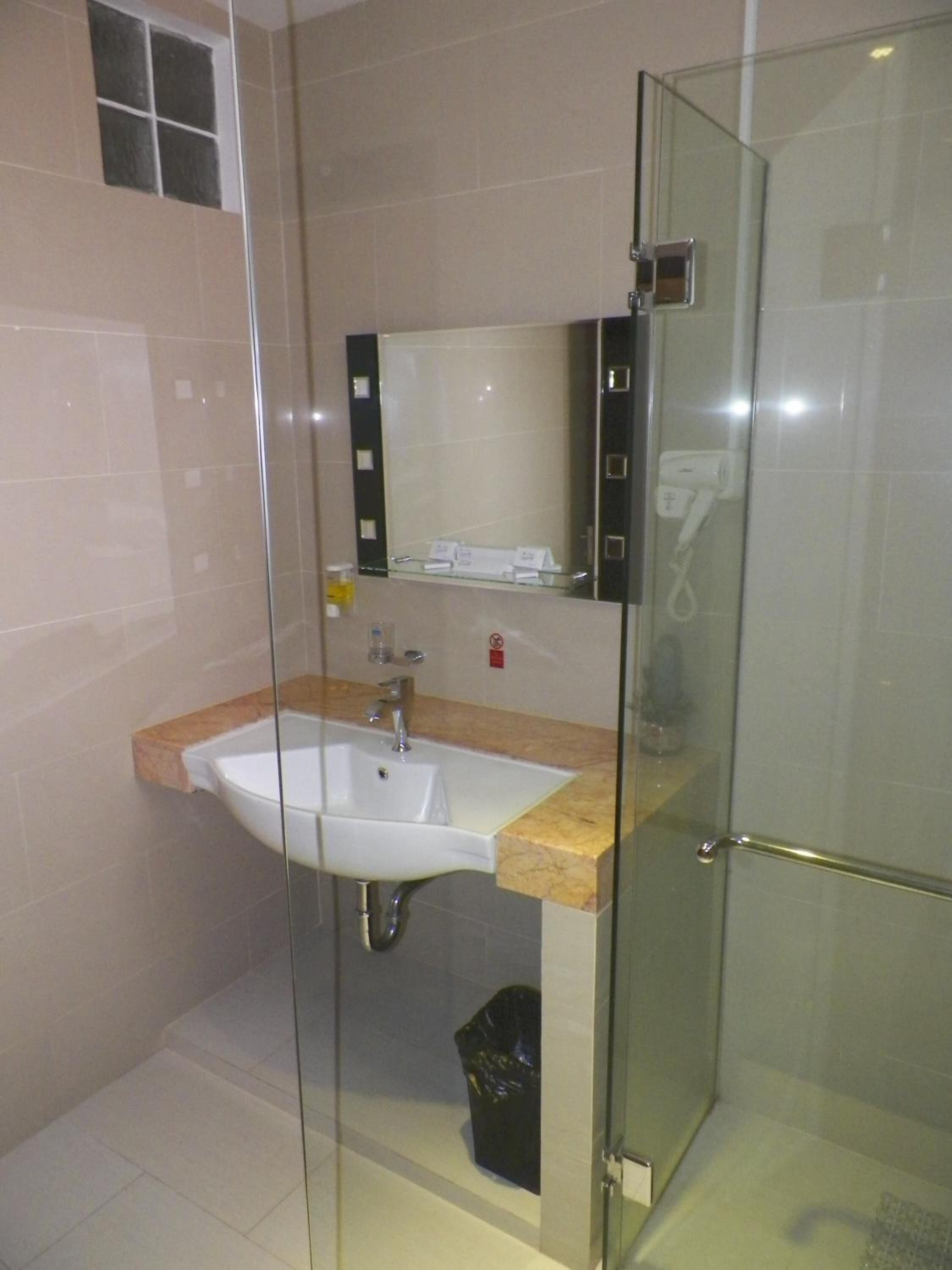 Uma casa de banho moderna com cabine de duche em vidro, uma pia com bancada de mármore e um espelho sobre a pia.